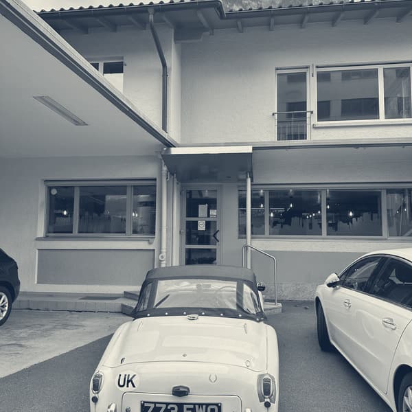 TS2 parked outside a cafe, hood up, a modern hatchback alongside and mountains in cloud above the roofline