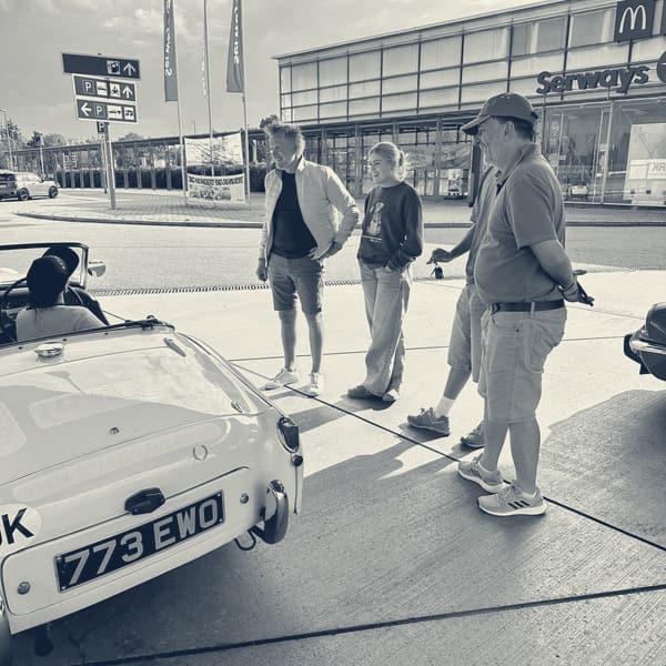 Three people and a girl in a blue jumper standing talking beside TS2 at a German service station, her number plate 773 EWO in the foreground