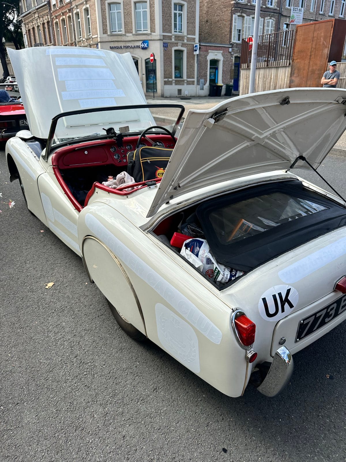 TS2 at the kerb in Amiens with both her bonnet and boot lid standing open, luggage visible in the boot, town houses behind