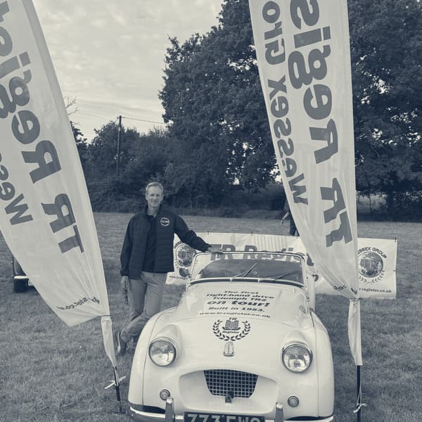 Andy standing beside TS2 in a field, a TR Register Wessex Group flag either side of the car