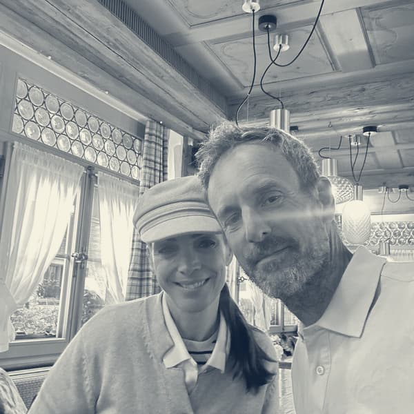 Evie and Andy cheek to cheek at the breakfast table, timber ceiling and leaded windows behind, Andy in his 10CR polo