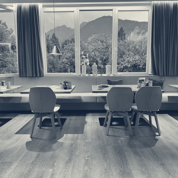 The hotel breakfast room, long banquette and set tables under a run of windows filled with mountain