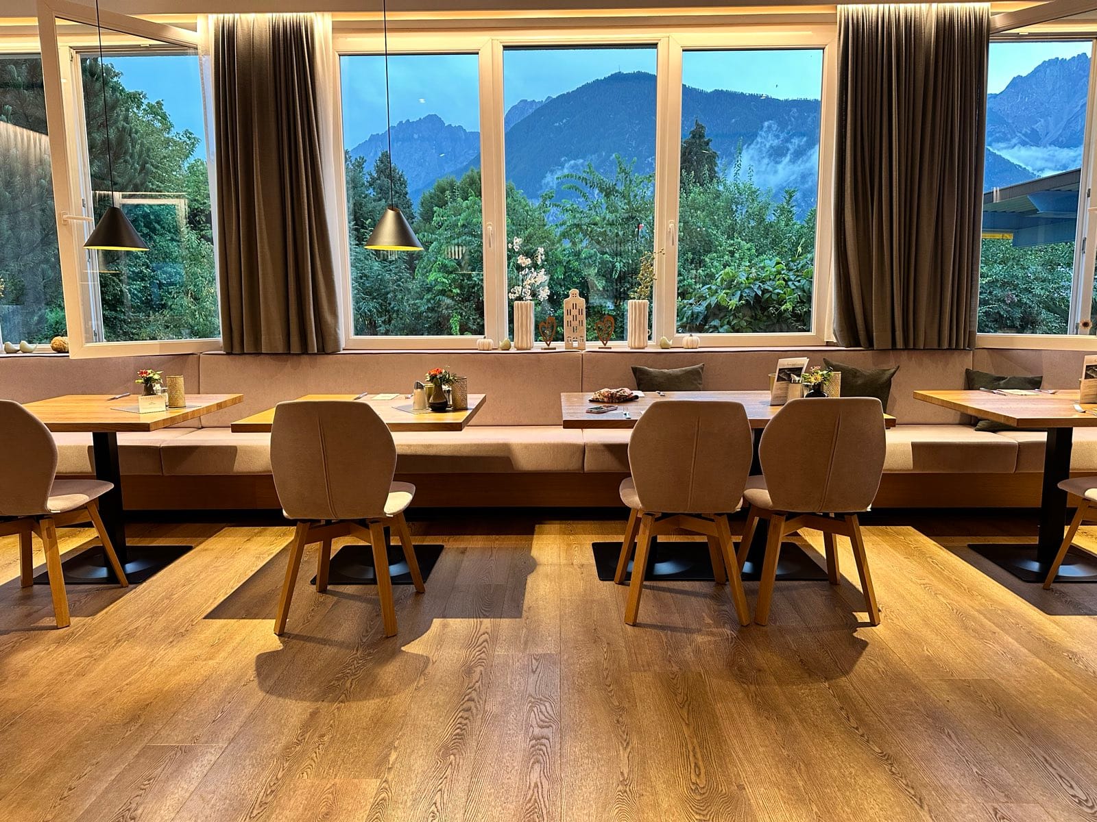 The hotel breakfast room, long banquette and set tables under a run of windows filled with mountain