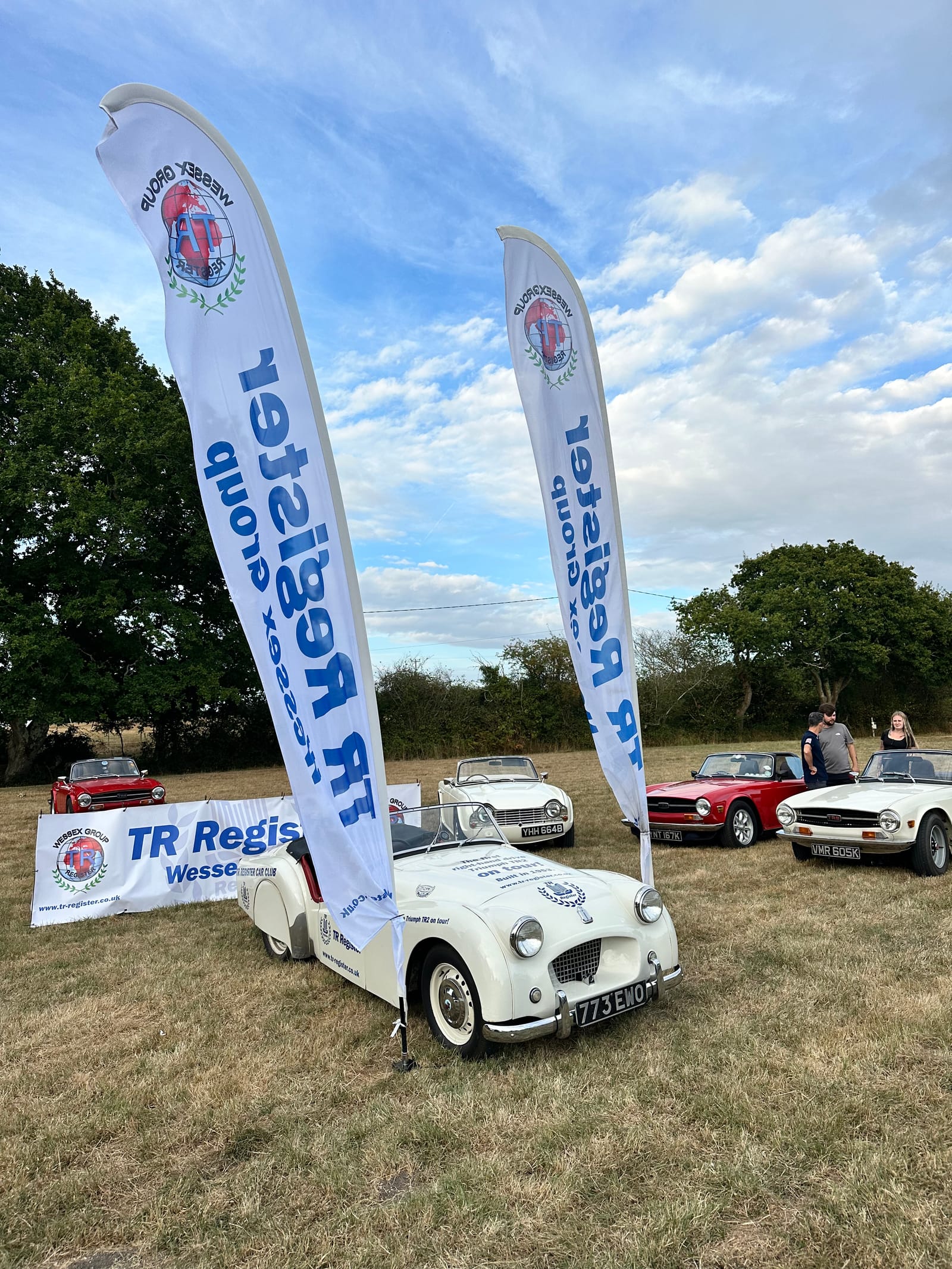 TS2 head on between two tall TR Register Wessex Group flags, the club banner behind and a row of later TRs to one side