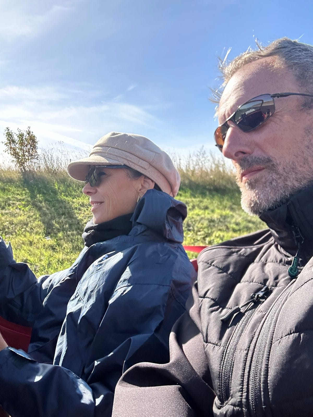 Evie and Andy side by side in TS2 in low sun, both in sunglasses, hedges and a field going past