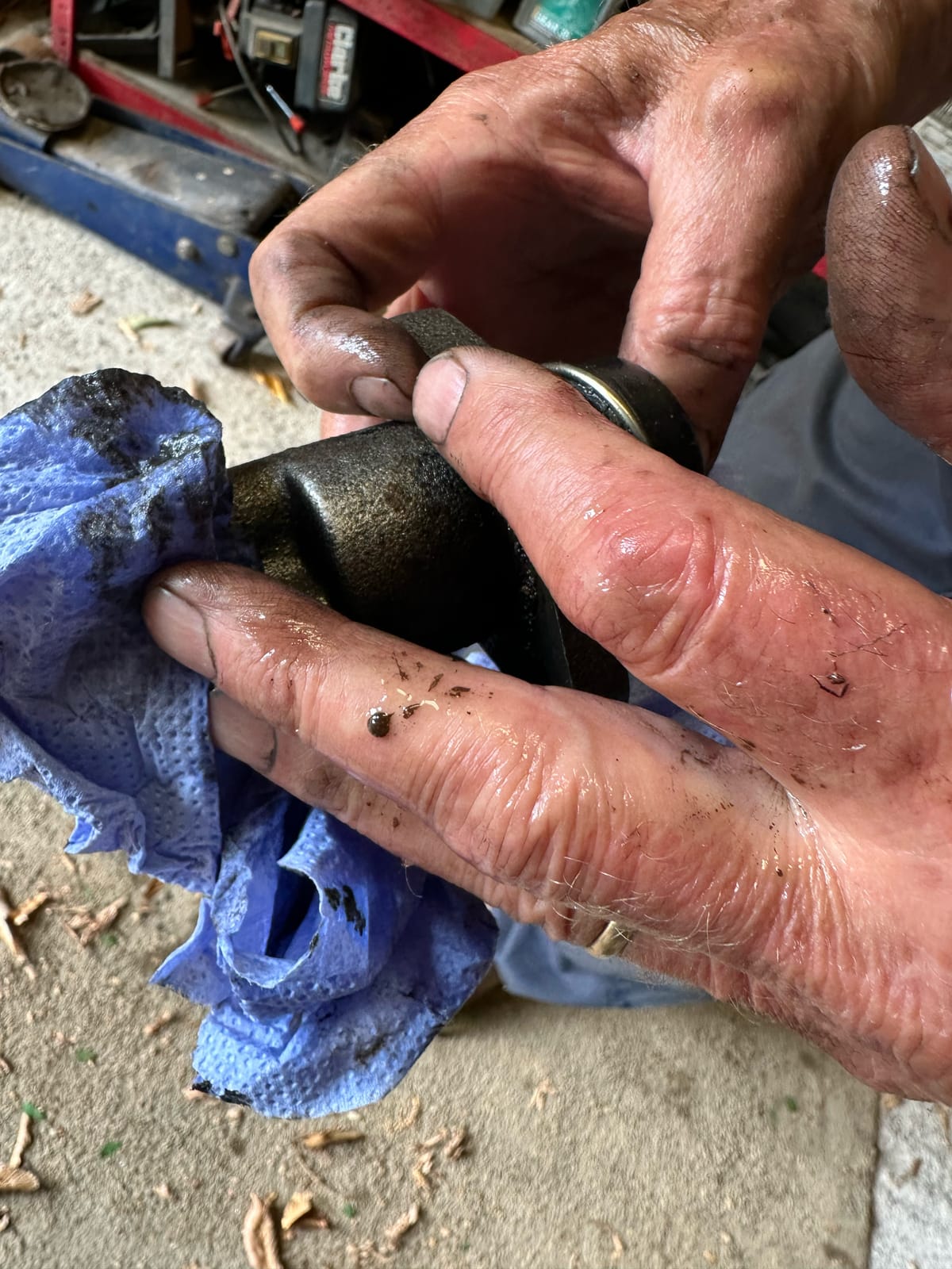 Oily hands wiping the old clutch slave cylinder on a blue paper towel, dark specks visible in the fluid