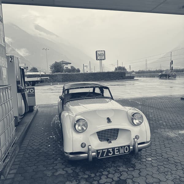 TS2 with her hood up under a filling station canopy, wet forecourt and a rain-grey valley behind