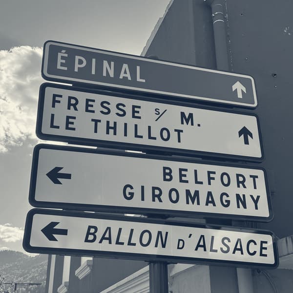 French road signs on a red-painted wall: Épinal straight on, Belfort and the Ballon d'Alsace to the left