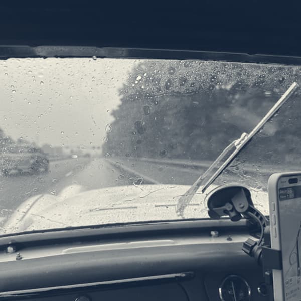 The view out of TS2's windscreen in the rain, wiper part way across, the phone on its mount showing the route, red dashboard below