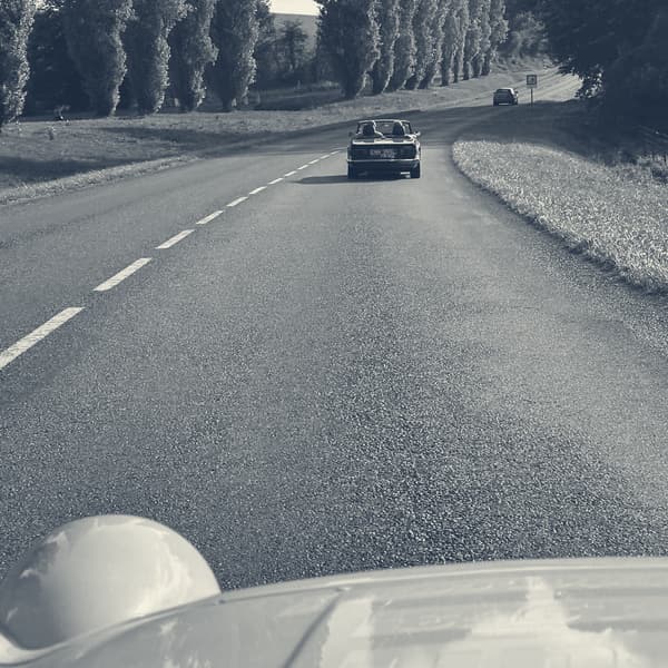 The view forward over TS2's bonnet down an avenue of poplars, a dark red TR6 ahead on the empty road