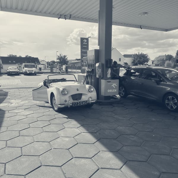 TS2 parked nose in under the canopy of a German filling station, hood down, a red hatchback at the next pump