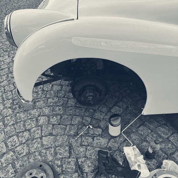 TS2's front wing with the wheel off, the hub lying on the cobbles beside a tin of brake fluid and a spread of tools