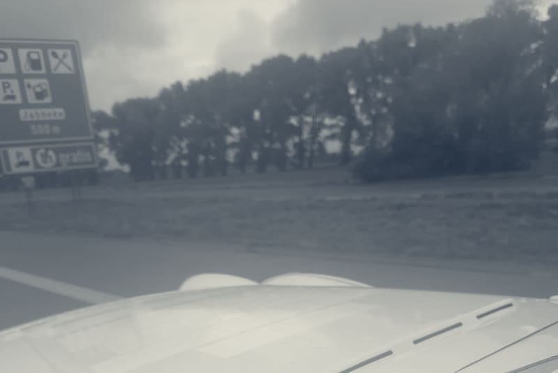TS2's white bonnet in the rain on the Belgian motorway, a blue services sign ahead reading Jabbeke 500 m