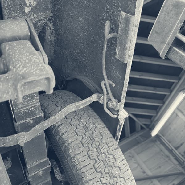 The brake backplate and its linkage exposed, the wheel leaning against the car beside it