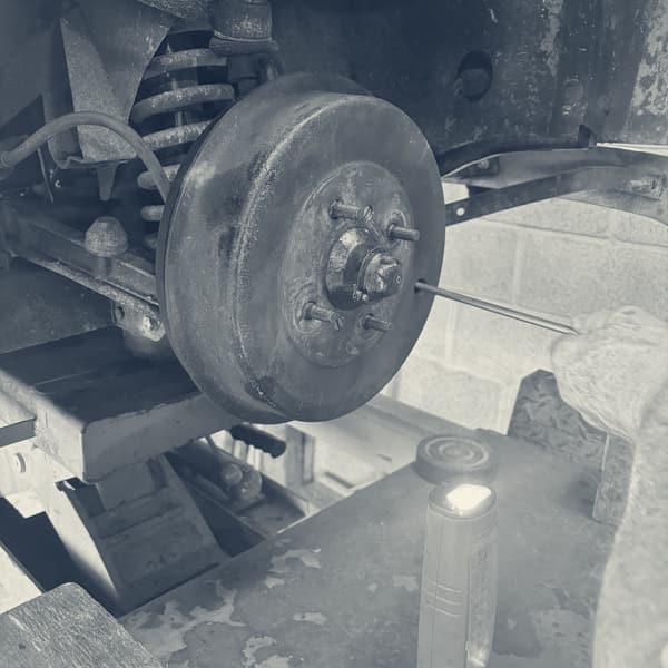 The front brake drum with the wheel off, coil spring above it, a torch lying on the bench below