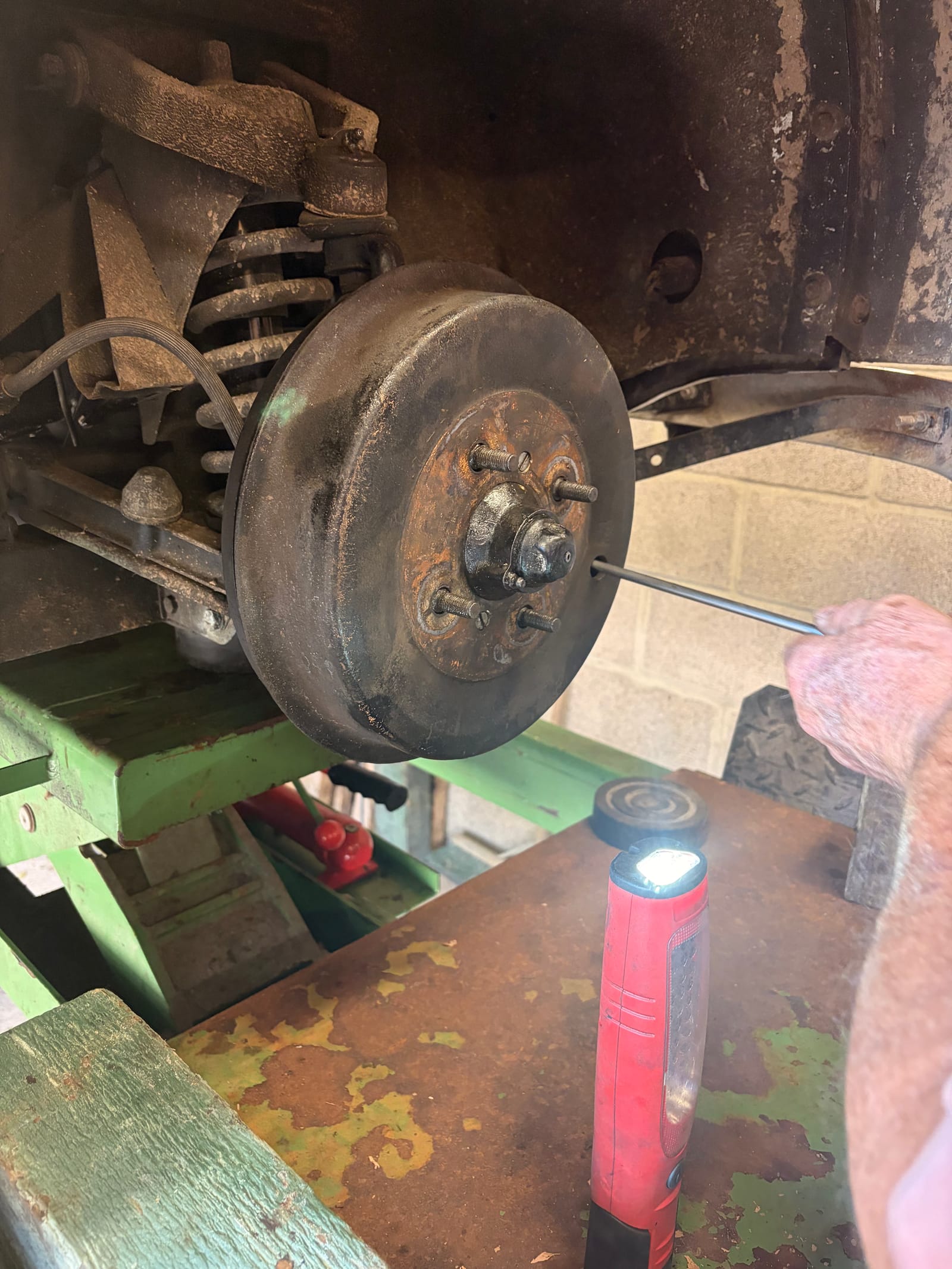 The front brake drum with the wheel off, coil spring above it, a torch lying on the bench below