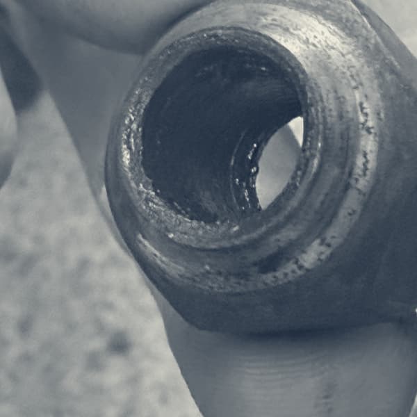 A wheel nut held up to the camera, looking down the bore at a thread worn smooth