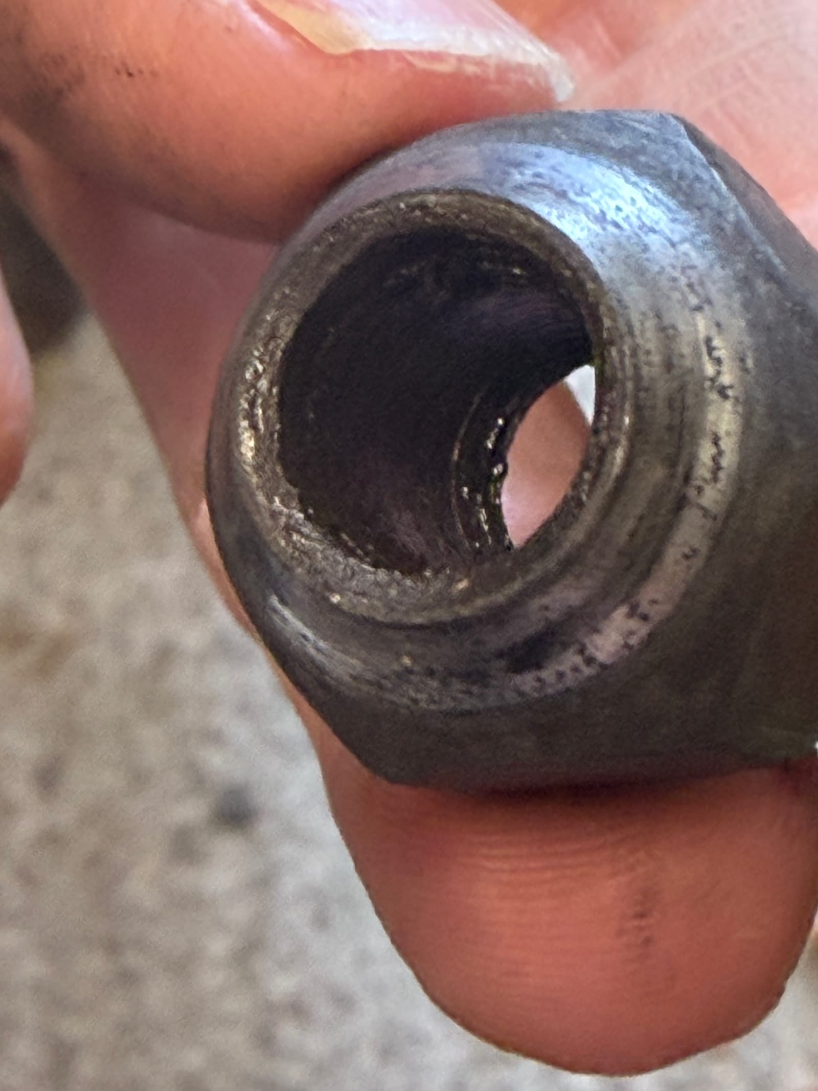 A wheel nut held up to the camera, looking down the bore at a thread worn smooth
