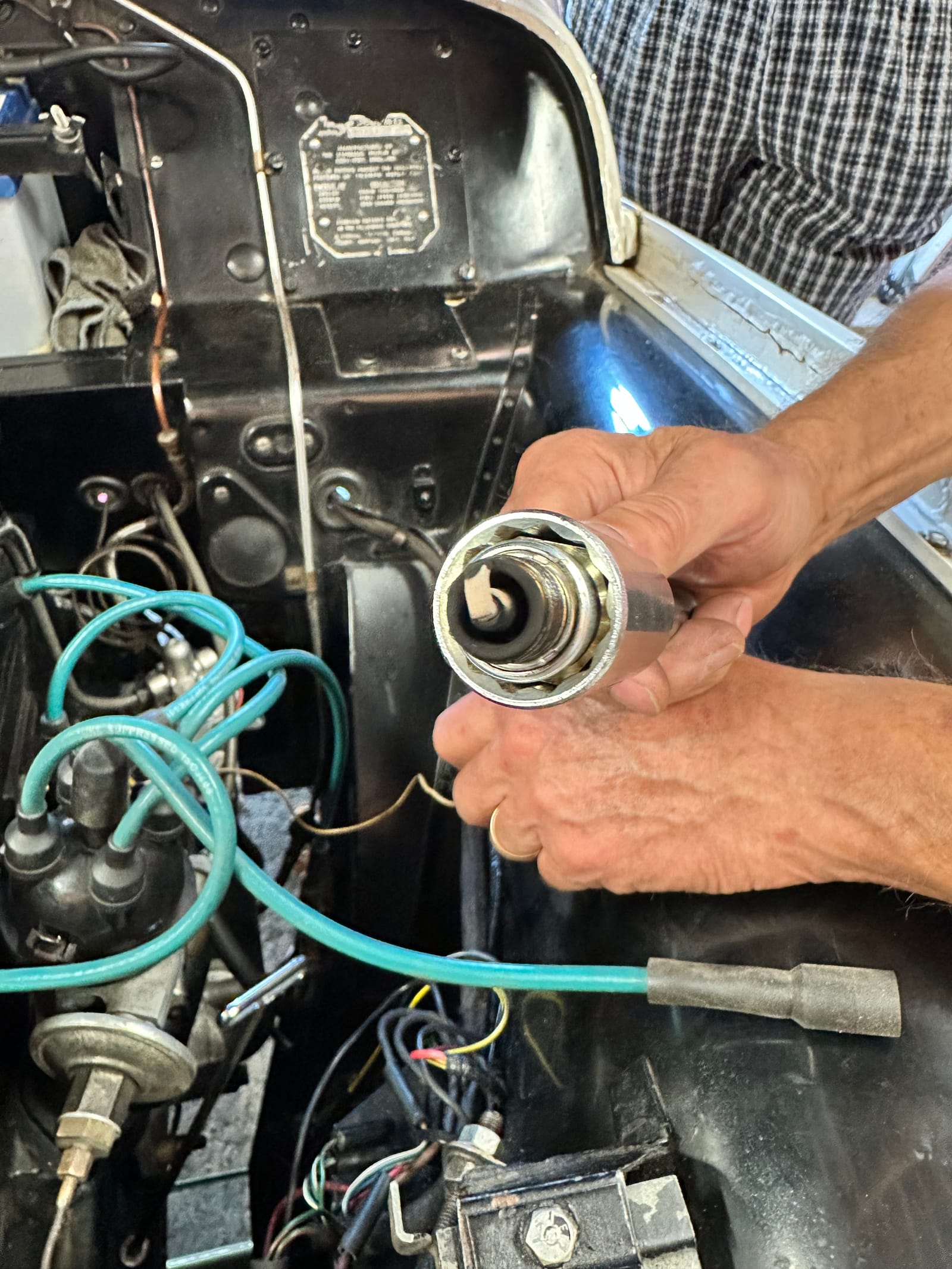 A spark plug just out of the head, held up beside the engine, its nose almost white