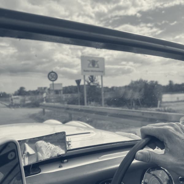 The Baden-Wurttemberg boundary sign with its three lions, seen through TS2's windscreen with a hand on the wheel and the dials below