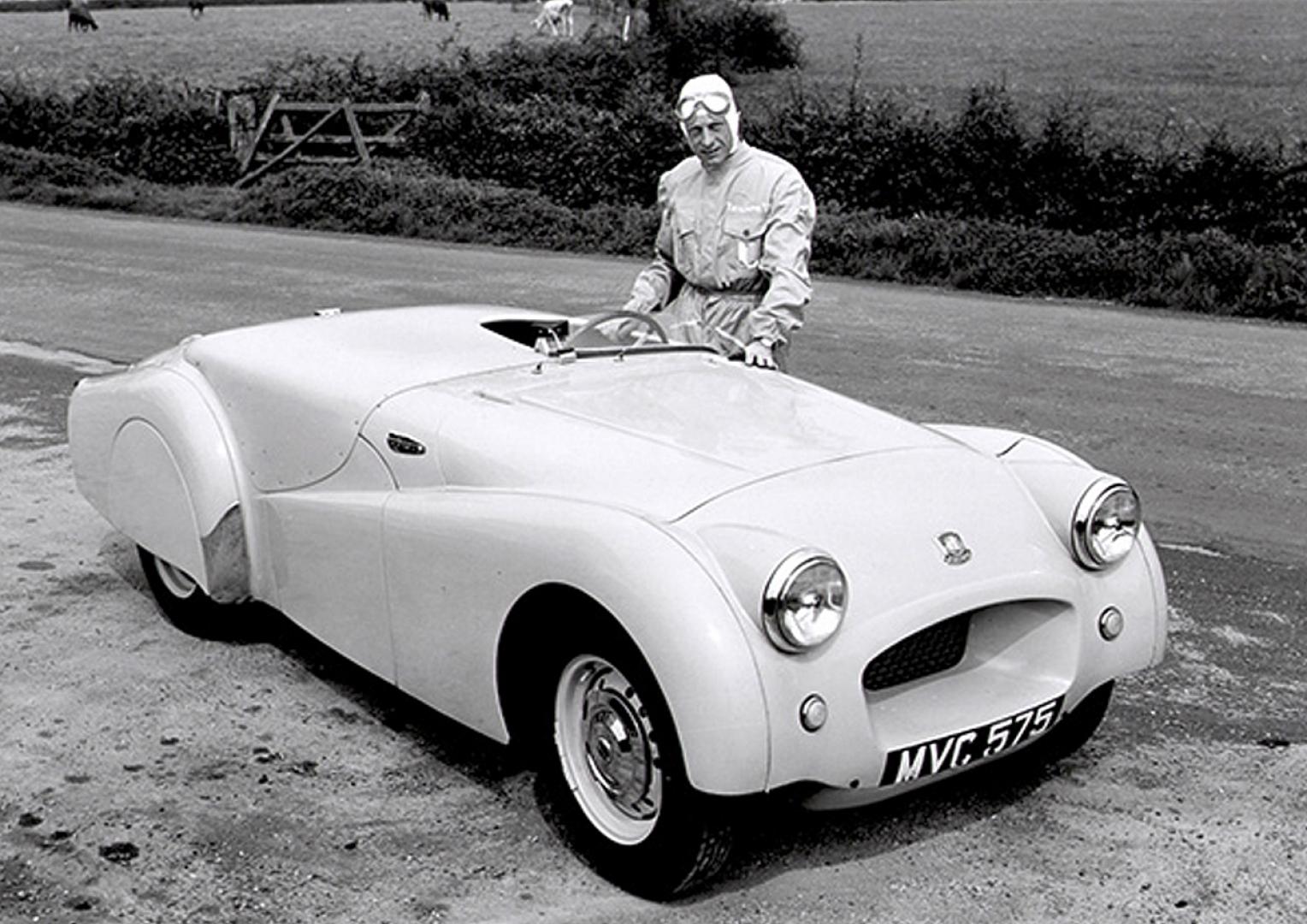 Ken Richardson in white overalls and helmet standing beside MVC 575, the streamlined pre-production TR2, on the Jabbeke road in 1953