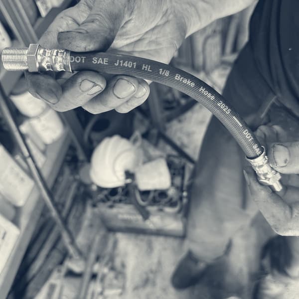 A new flexible hose held up in both hands, the moulded lettering reading DOT SAE J1401 HL one eighth Brake Hose 2025