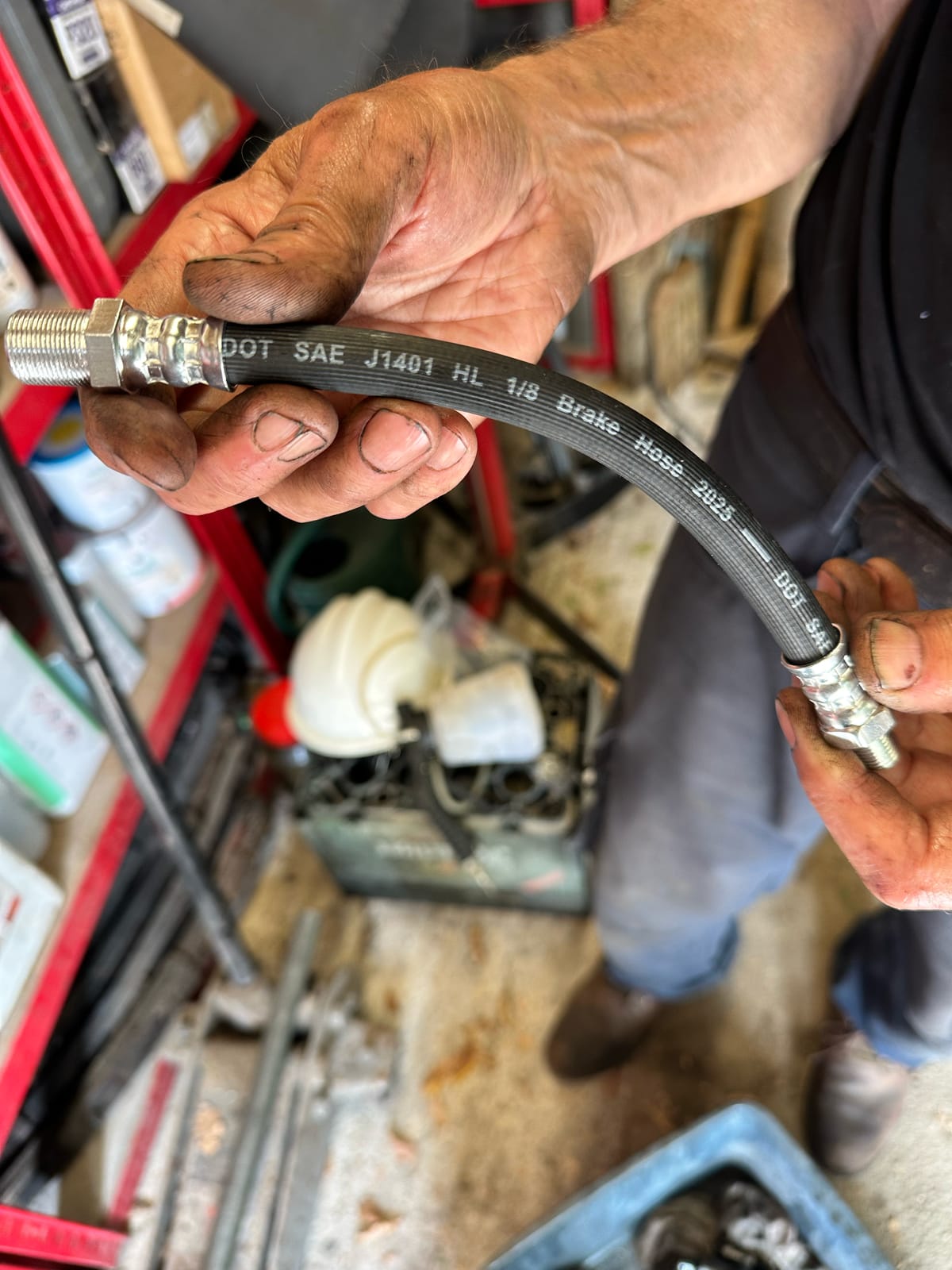 A new flexible hose held up in both hands, the moulded lettering reading DOT SAE J1401 HL one eighth Brake Hose 2025