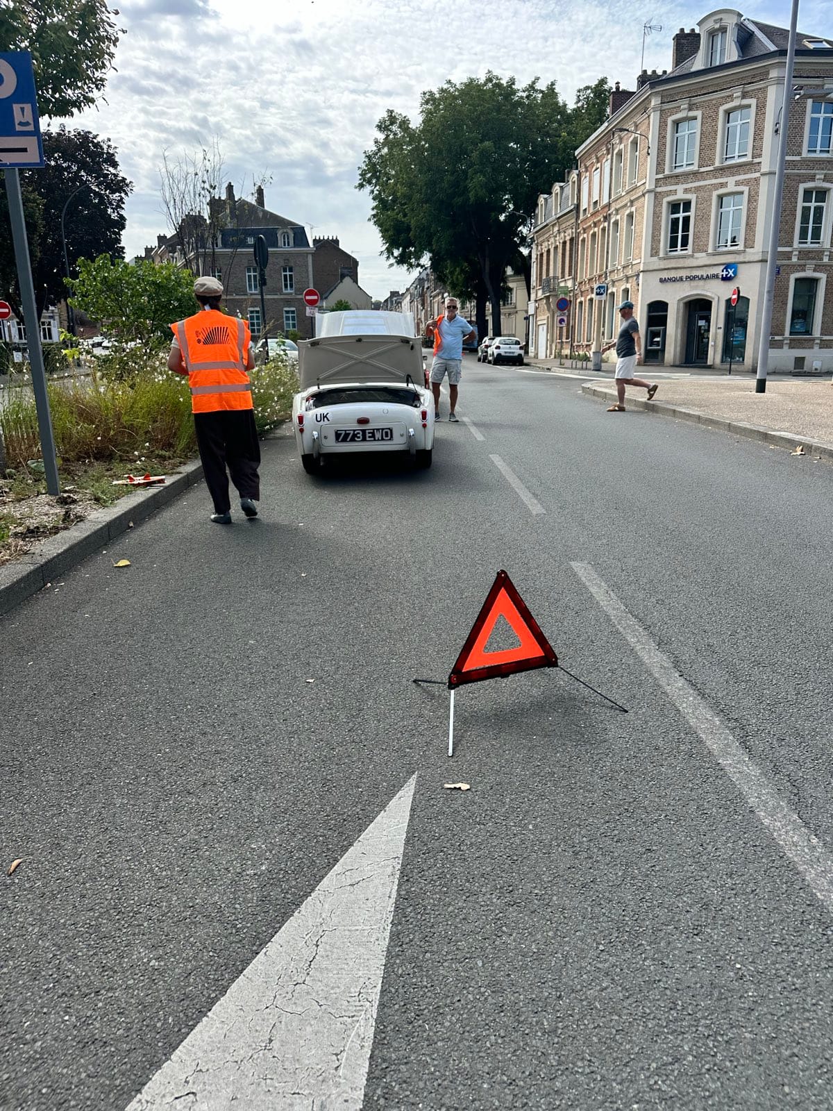 A red warning triangle standing in the middle of an Amiens street, TS2 stopped ahead of it with her bonnet up and a figure in a hi-vis vest walking back