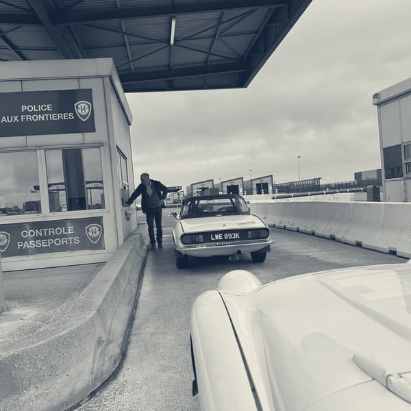 A Police aux Frontieres booth at Dunkirk marked Controle Passeports, another entrant's Triumph saloon at the window ahead, TS2's white wing in the corner