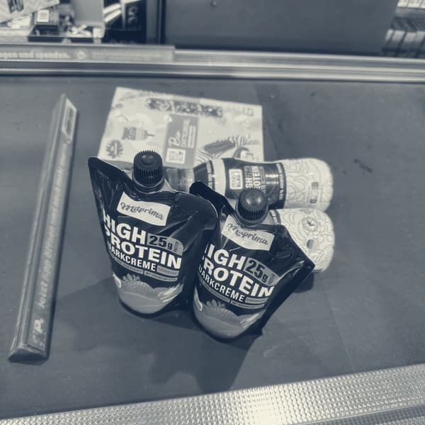 Two strawberry high protein pouches, a chocolate bar and two drinks on a German supermarket checkout belt