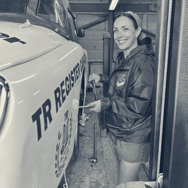 Evie smiling beside TS2 up on the four post lift, torque wrench in hand, the car's roof still on
