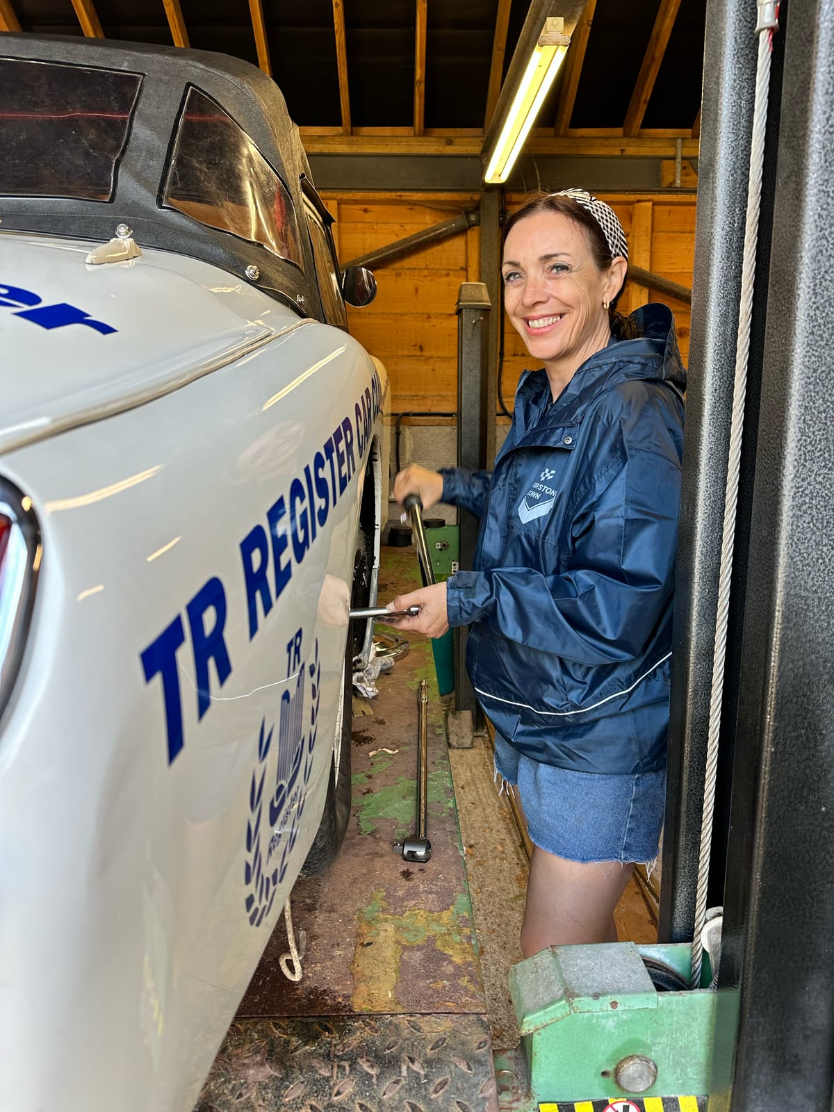 Evie smiling beside TS2 up on the four post lift, torque wrench in hand, the car's roof still on