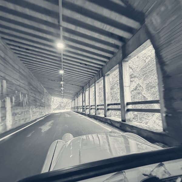 Inside an open-sided avalanche gallery on the Stelvio descent, concrete pillars down one side and the valley beyond