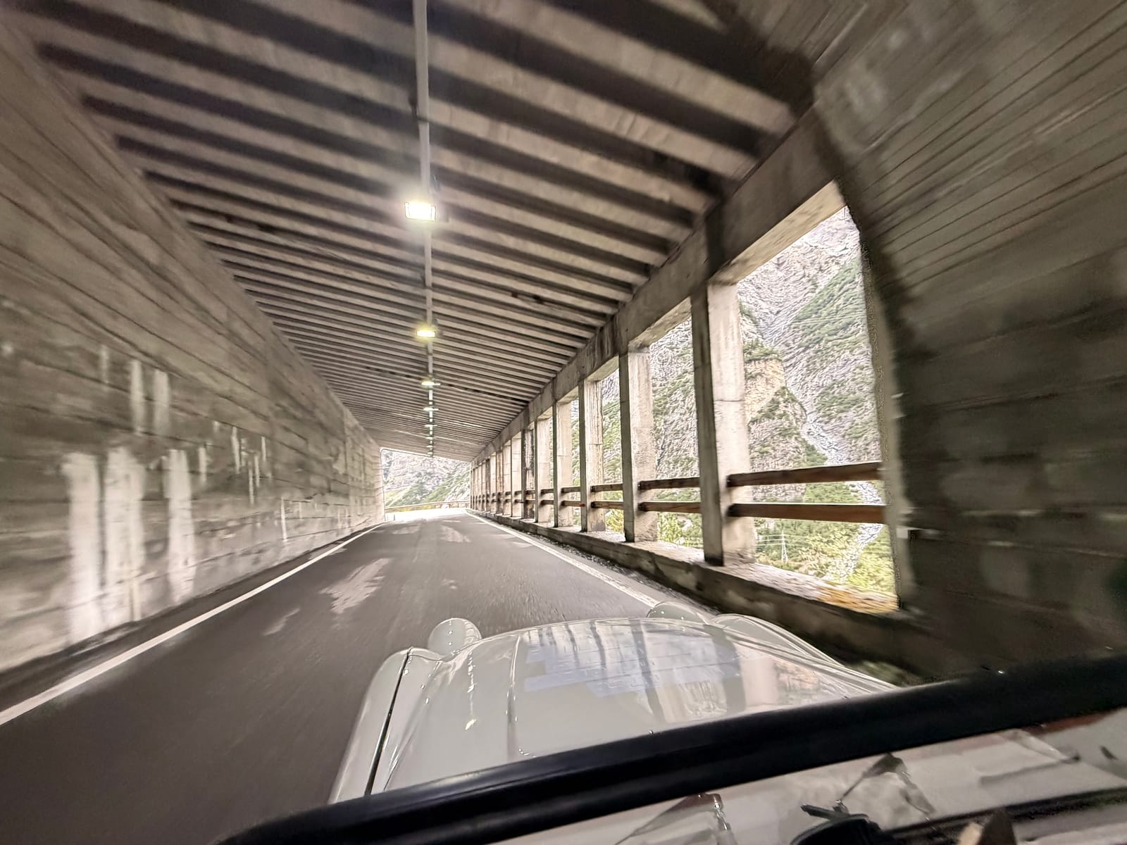 Inside an open-sided avalanche gallery on the Stelvio descent, concrete pillars down one side and the valley beyond