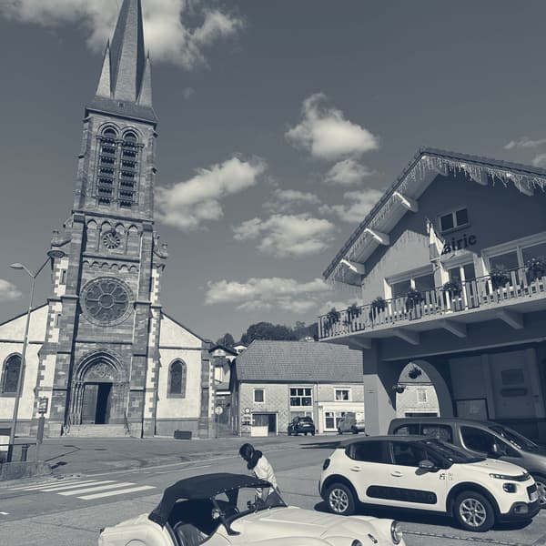 The red sandstone church at Saint-Maurice-sur-Moselle under a blue sky, TS2 parked at the kerb below and Evie climbing in