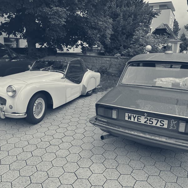TS2 and a blue Triumph Dolomite parked nose to tail on the hotel car park in Andermatt, first light on the hills behind