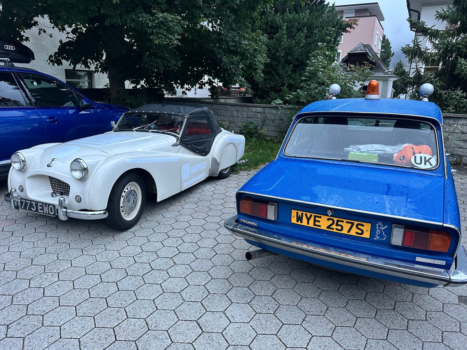 TS2 and a blue Triumph Dolomite parked nose to tail on the hotel car park in Andermatt, first light on the hills behind