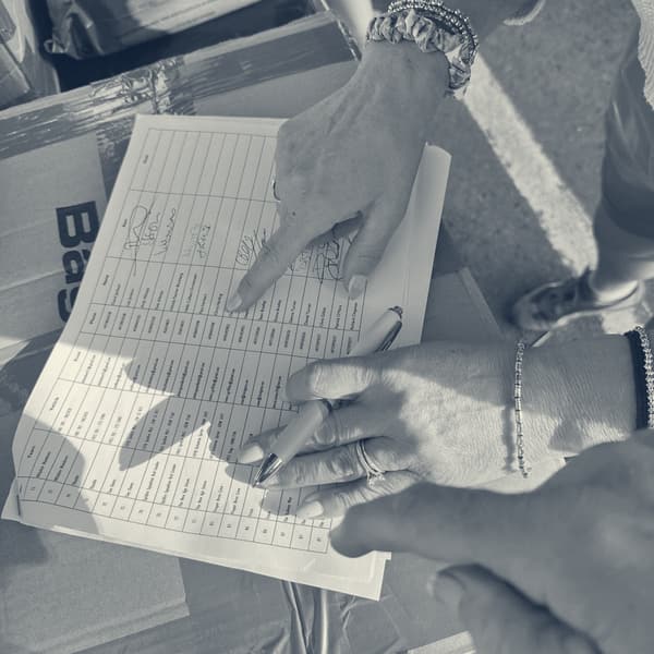 Two pairs of hands over the printed start list, one pointing at a line, the other holding a pen, the sheet resting on a cardboard box