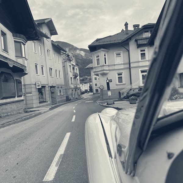 A quiet town street of pink and yellow houses, seen past TS2's windscreen frame