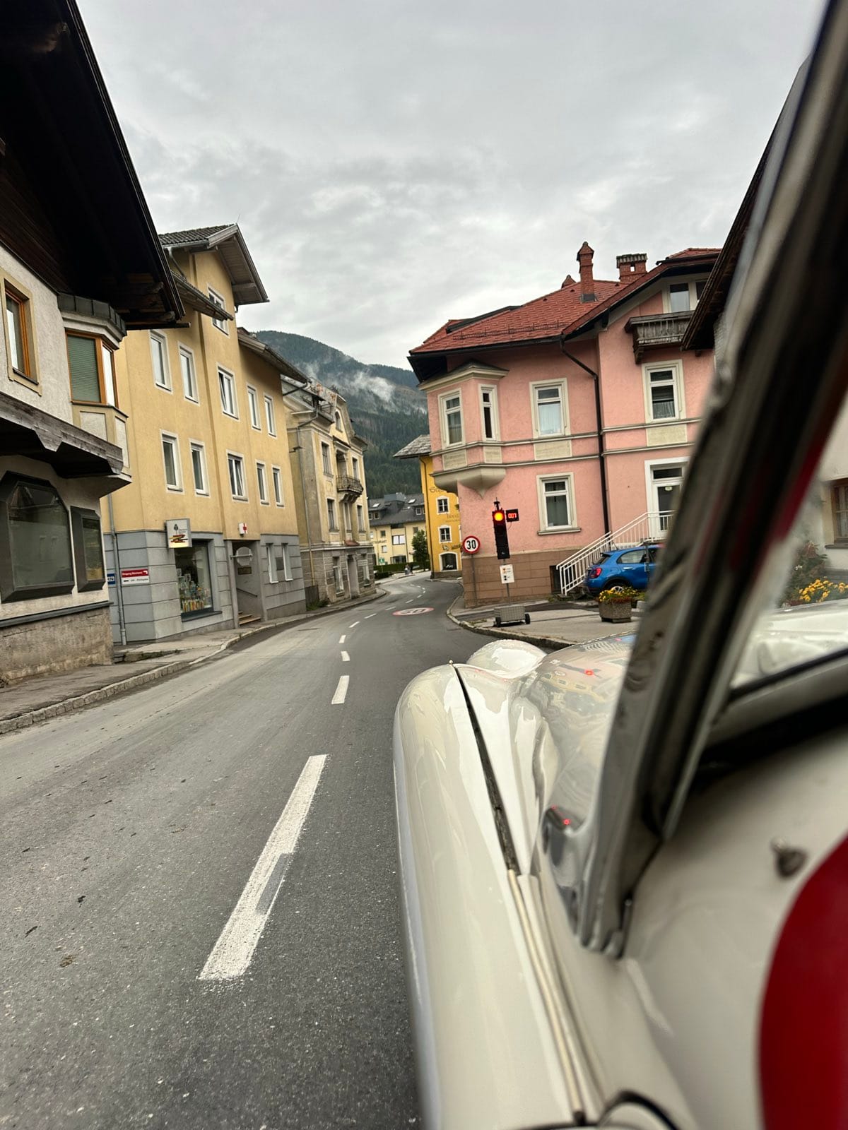 A quiet town street of pink and yellow houses, seen past TS2's windscreen frame