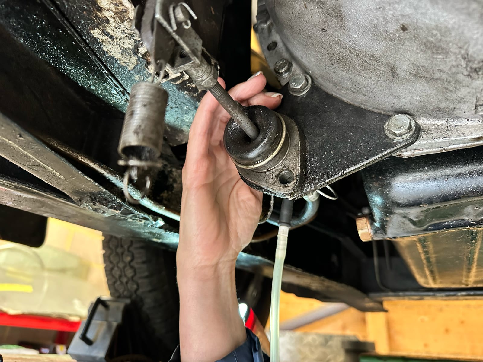 A hand reaching up to the clutch operating rod and its rubber boot on the underside of the gearbox bellhousing
