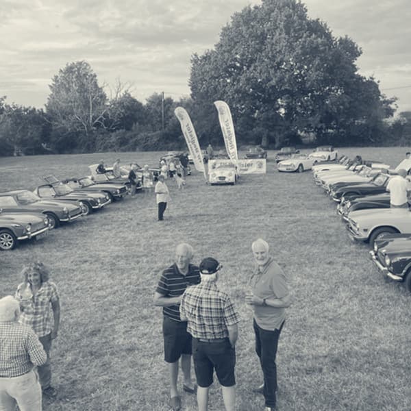 The same field later in the evening, members standing about in groups with drinks as the light goes