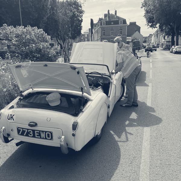 TS2 stopped at the side of an Amiens boulevard with her bonnet and boot lid up, Andy in a hi-vis vest leaning in over the door, a cap left on the rear deck