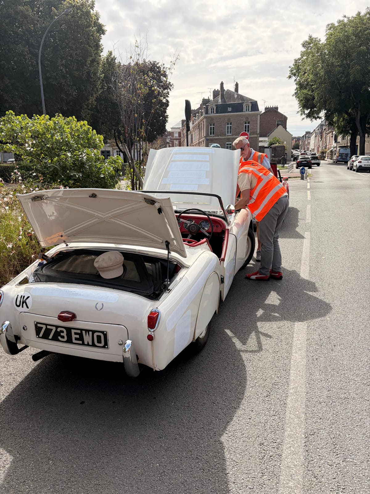 TS2 stopped at the side of an Amiens boulevard with her bonnet and boot lid up, Andy in a hi-vis vest leaning in over the door, a cap left on the rear deck