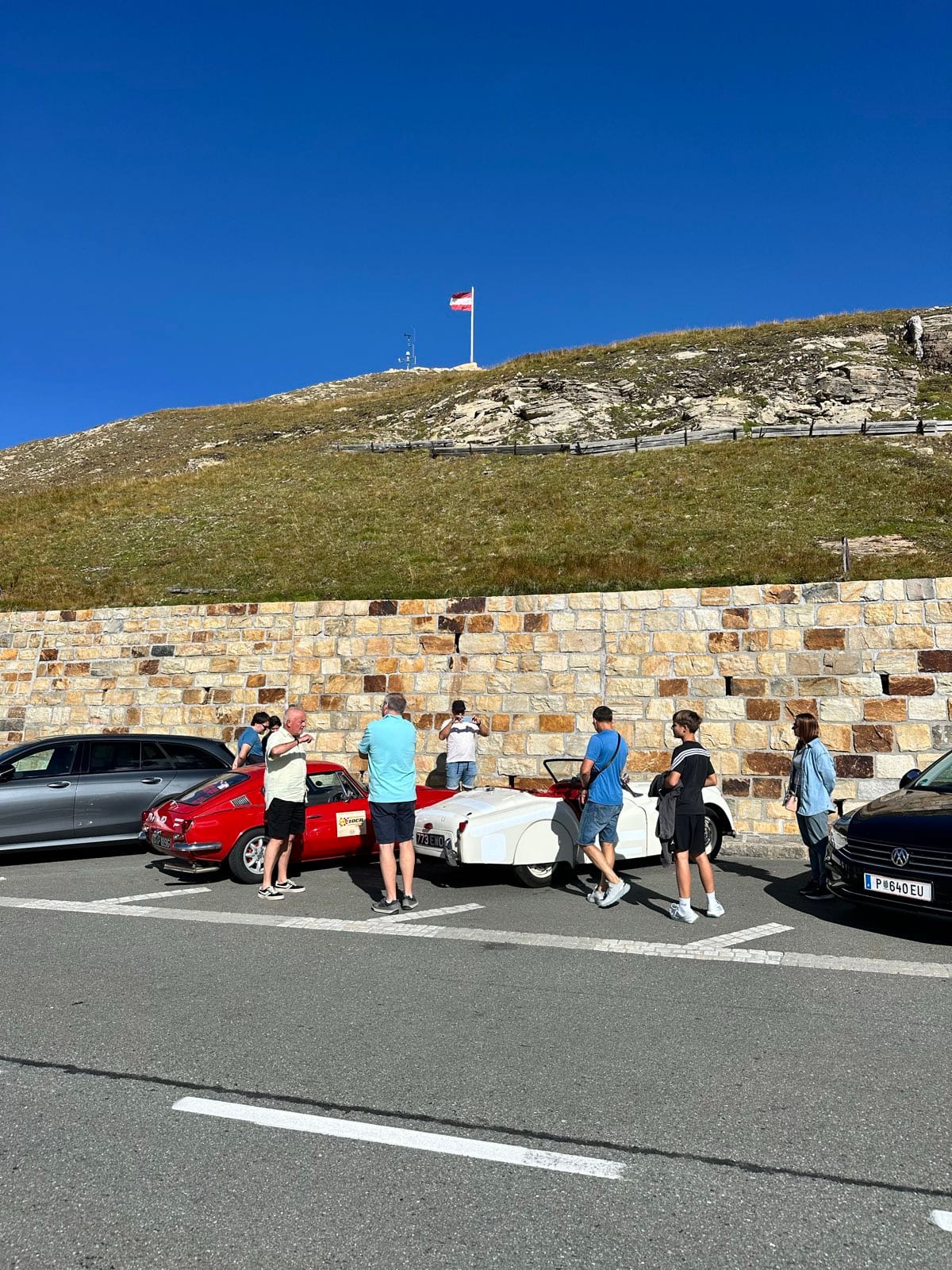 People standing around the parked cars at the summit, several photographing TS2