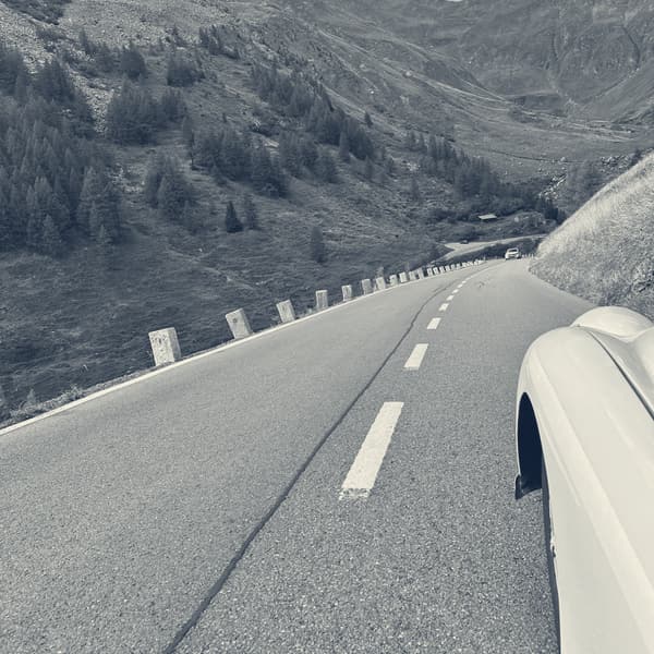 The road dropping away between larches and crash barriers, a long valley opening ahead