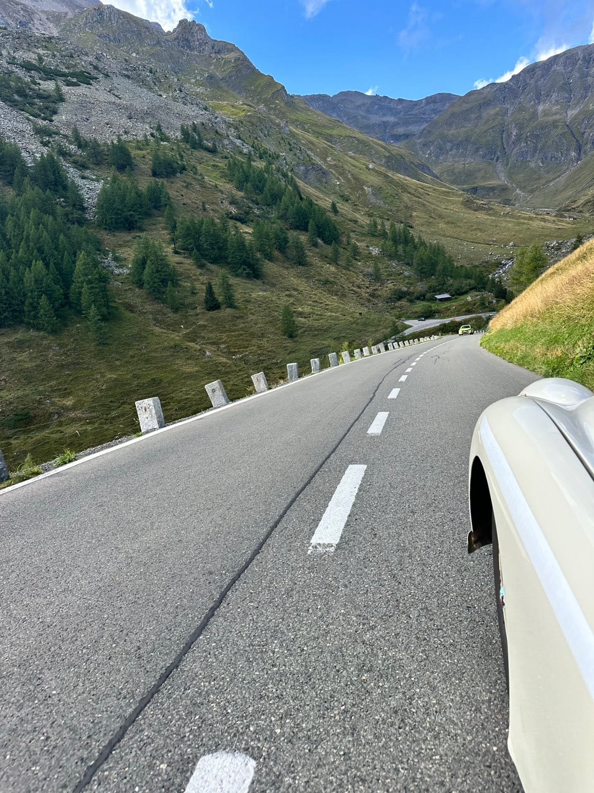 The road dropping away between larches and crash barriers, a long valley opening ahead