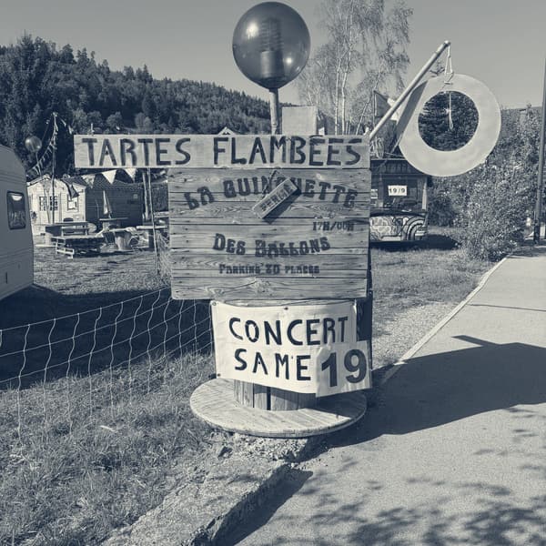 A hand-painted wooden sign for tartes flambées at La Guinguette des Ballons, a concert chalked up for the nineteenth, no one about