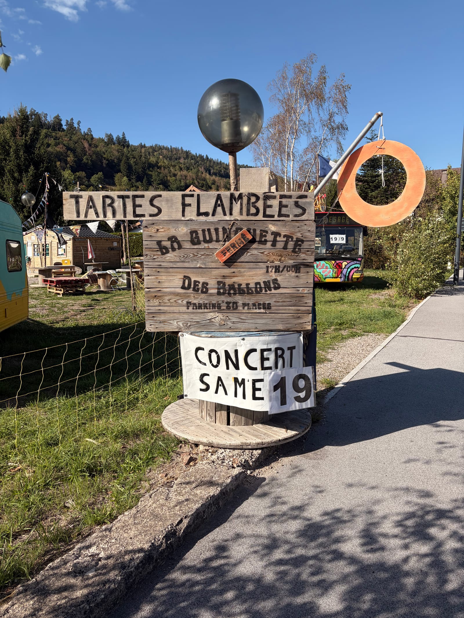 A hand-painted wooden sign for tartes flambées at La Guinguette des Ballons, a concert chalked up for the nineteenth, no one about