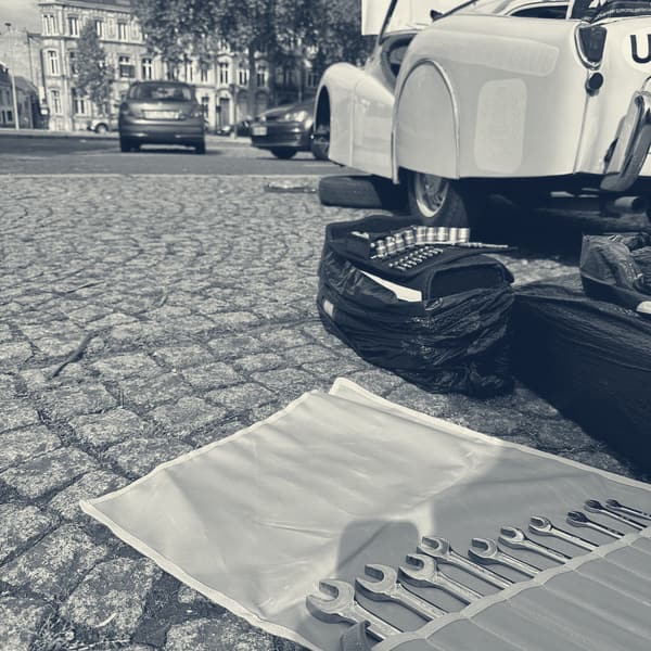 A spanner roll opened out on the cobbles with a socket set and tool bags beside it, TS2's tail and open boot behind